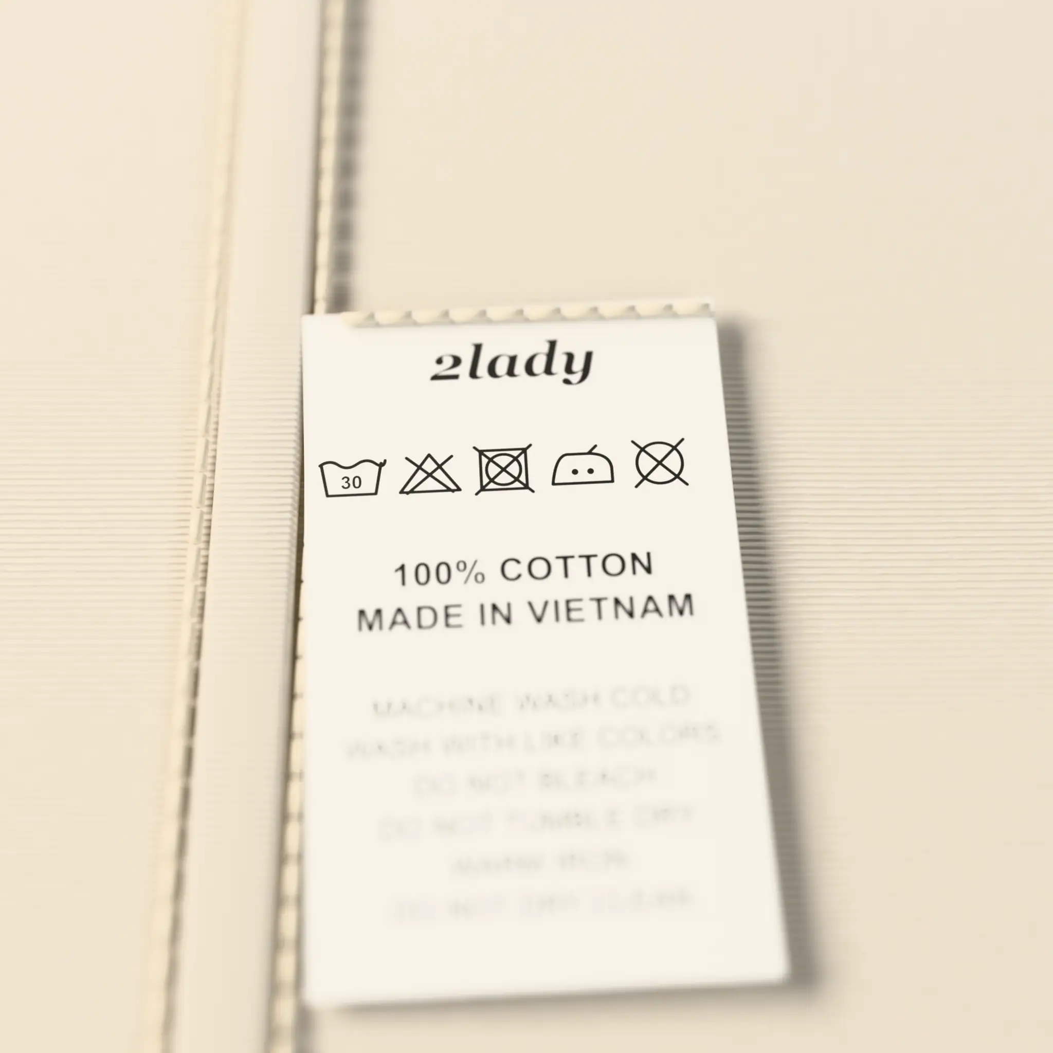 White satin care label sewn into a side seam: the 2lady wordmark, laundry symbols, 100% cotton, made in Vietnam